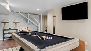 Une table de billard avec des billes, un canapé, un téléviseur et un escalier.