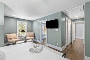 A modern bedroom with a bed, two chairs, a TV, and a hallway. - Modern Villa w Pool, Hot Tub & Games! (Greensboro)