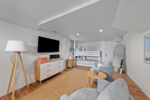 A modern living room with a TV, sofa, and a bunk bed in the background.