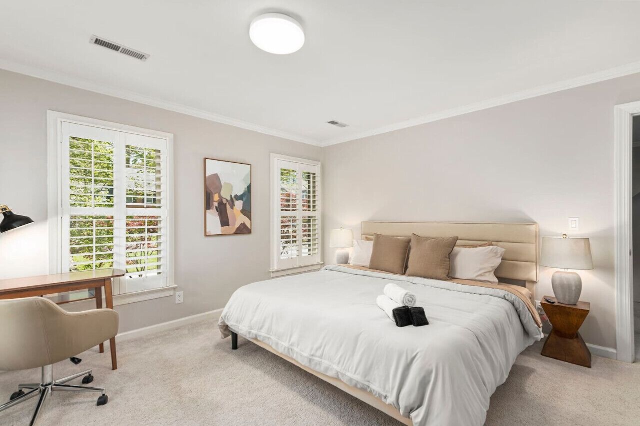 A bedroom with a bed, a desk, and two windows with blinds.