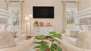 A cozy room with bunk beds, a flat-screen TV, a bedside table with books, and a potted plant.