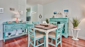 A dining area with teal chairs and a wooden table, a teal cabinet, and a white side table with a plant. - One Bedroom, 620 Sq Ft, Seacrest Beach, Free Bikes (Panama City Beach)