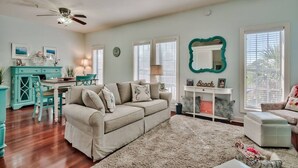 A spacious living room with a beige sofa, teal accent chair, and a dining area with a teal table. - One Bedroom, 620 Sq Ft, Seacrest Beach, Free Bikes (Panama City Beach)