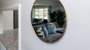 Un salon moderne avec un grand miroir ovale au mur, un canapé gris agrémenté de coussins à motifs et une grande plante en pot.