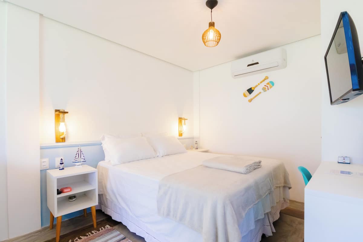 A neatly arranged hotel room with a bed, bedside tables, a desk, and a wall-mounted TV.