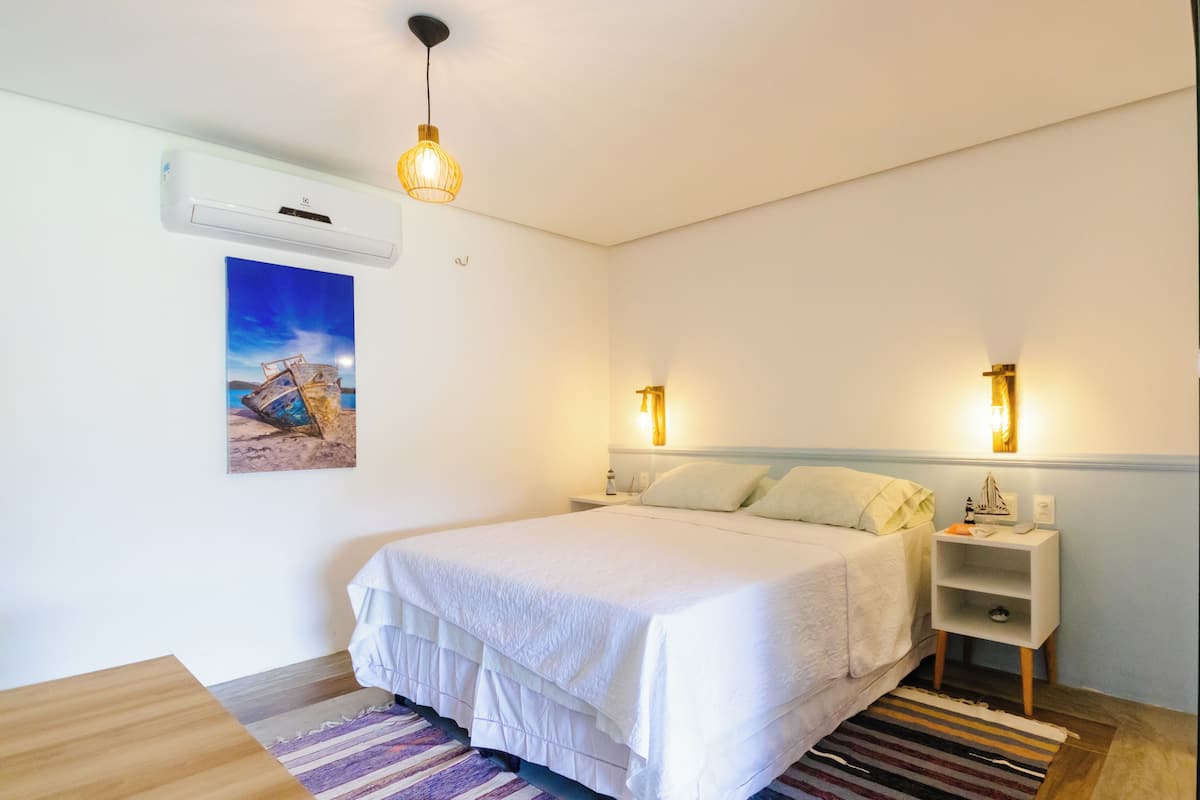A bedroom with a bed, bedside tables, a wall-mounted air conditioner, and a painting.