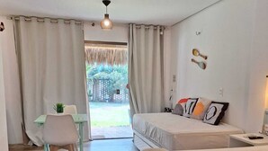 A bedroom with two beds, a desk, and a chair. There is a view of a garden through the window. - Summervilleflatsbg (Cajueiro da Praia)