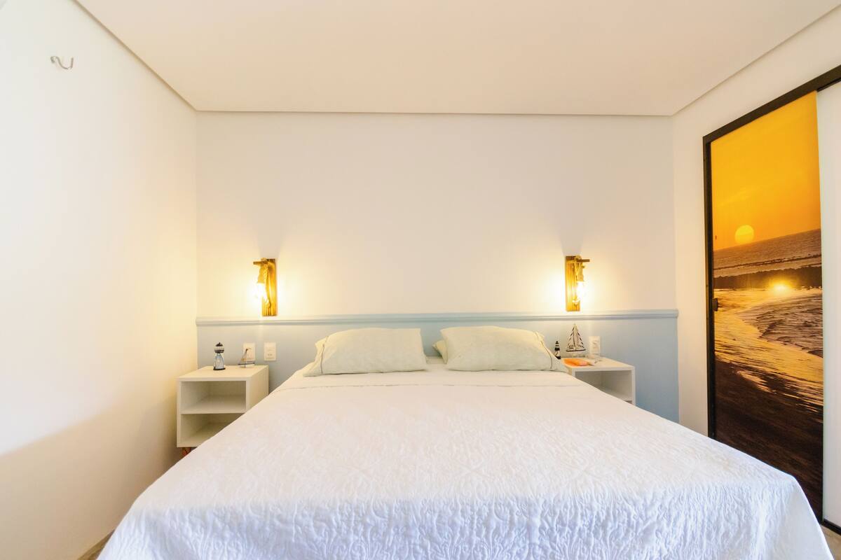 A bedroom with a large bed, two bedside tables, and a wall-mounted lamp.