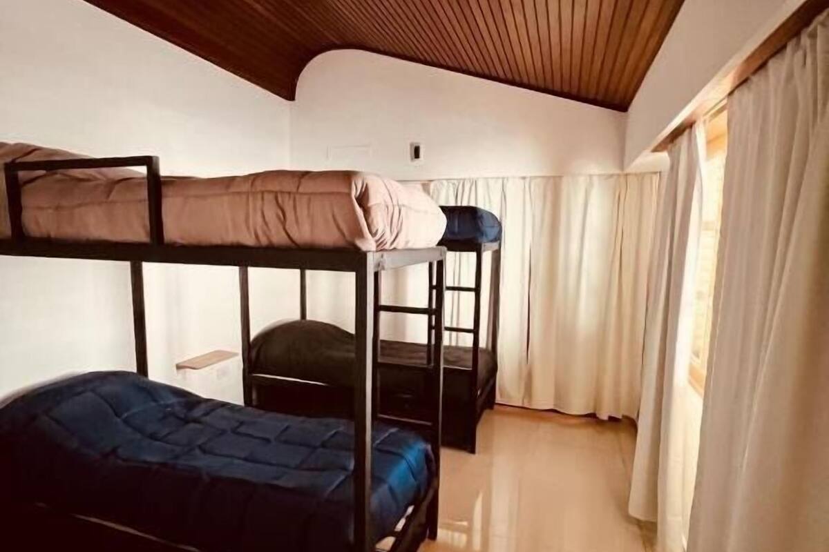 Una habitación con literas, techo de madera y una ventana con cortinas.