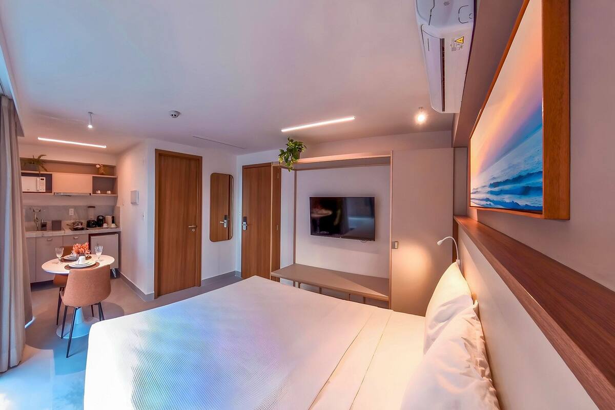 Une chambre d’hôtel moderne dotée d’un grand lit, d’un téléviseur fixé au mur, d’un petit coin repas et d’une kitchenette.