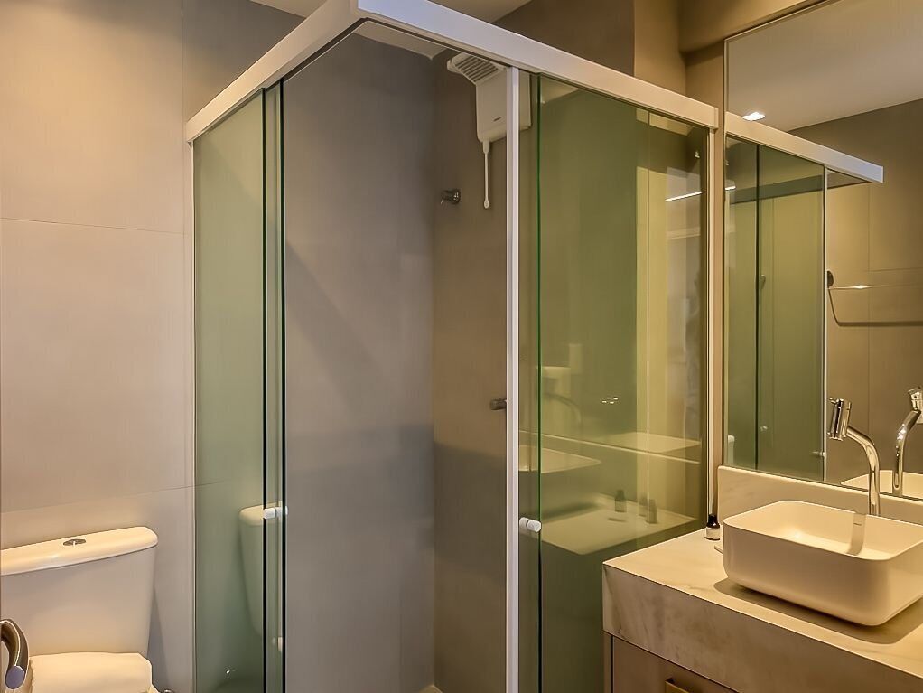 A modern bathroom with a glass shower enclosure, a toilet, and a sink with a mirror above it.