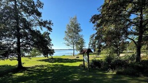 A grassy area with trees and a small structure, likely a gazebo, near a body of water. - Gård 2 hus, bastu, internet med fiber. Lugnt (Dannäs)
