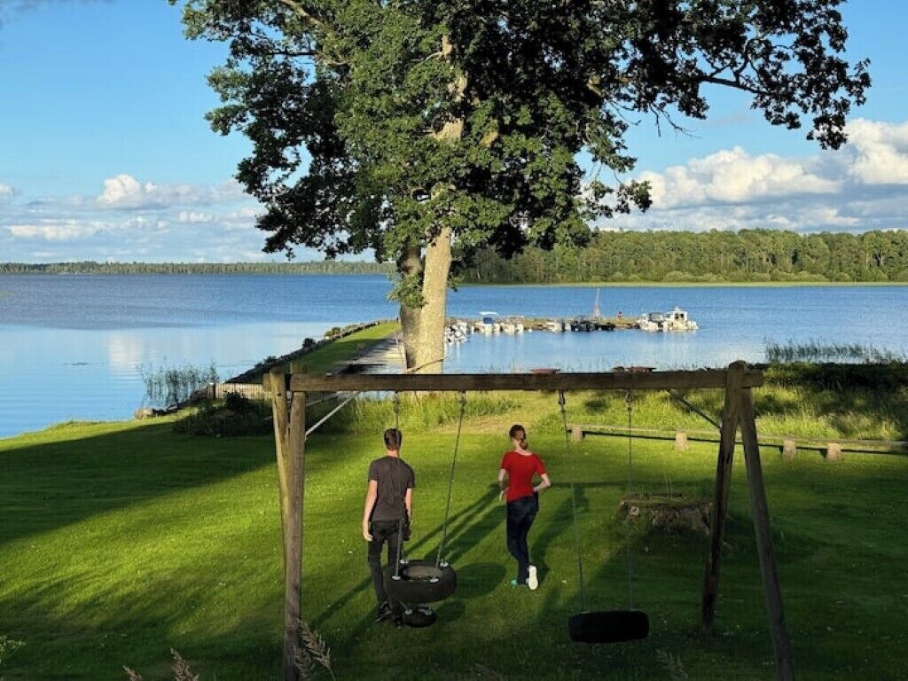 Une balançoire en bois avec deux sièges, une zone herbeuse et un lac en arrière-plan.
