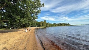 A sandy beach with a calm lake, trees, and a clear sky. - Gård 2 hus, bastu, internet med fiber. Lugnt (Dannäs)