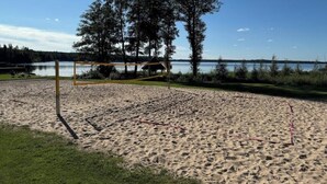 A sandy beach with a volleyball net, trees, and a body of water in the background. - Gård 2 hus, bastu, internet med fiber. Lugnt (Dannäs)