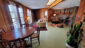 A rustic interior with a wooden dining table, chairs, a sofa, and a stone fireplace.
