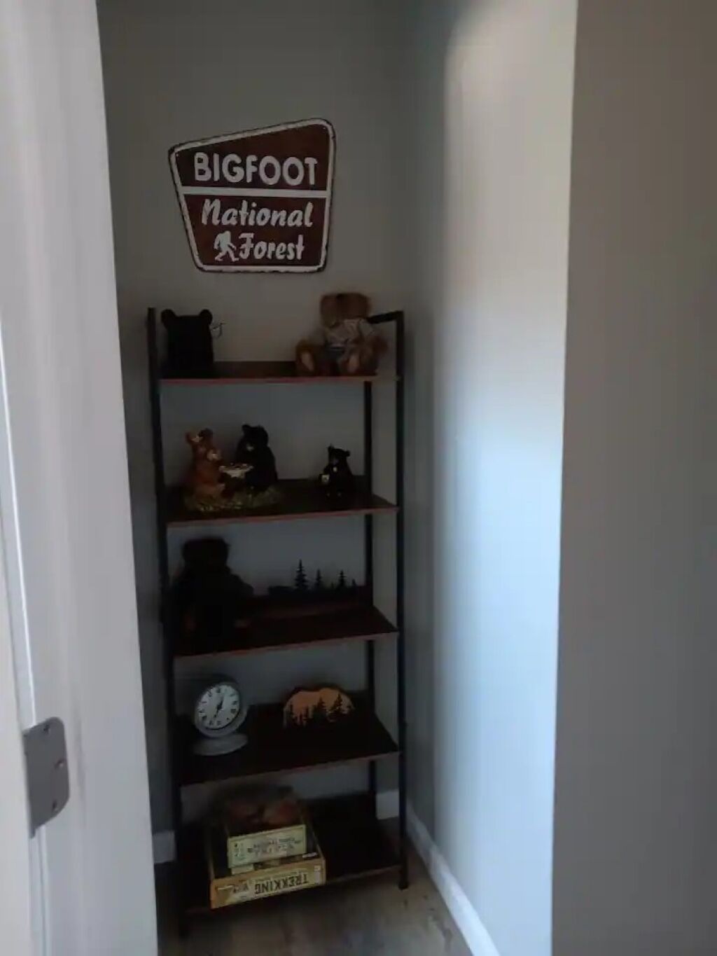 A hallway with a metal shelf unit displaying various items, including a clock and a sign that reads "BIGFOOT National Forest."