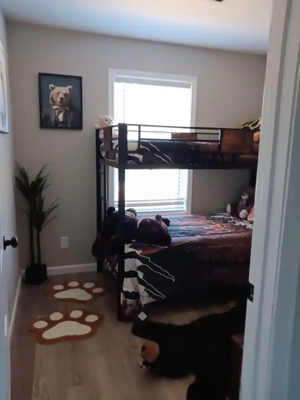 Habitación con literas, una ventana, un cuadro de un oso y una alfombra con huellas de pata.