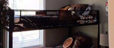 Dormitorio con literas, una ventana, un oso de peluche y una lámpara.