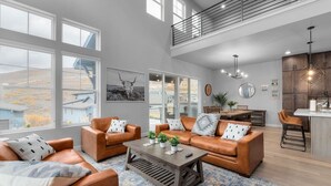 Uma sala de estar ampla com sofás de couro, uma mesa de centro e janelas grandes com vista para o exterior.