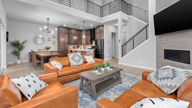 Uma sala de estar espaçosa com sofás de couro, uma mesa de centro e uma mesa de jantar com cadeiras. Uma escadaria leva a um andar superior com uma varanda.