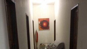 Un pasillo con suelo de baldosas, una cama, un cubo de basura y un cuadro en la pared.