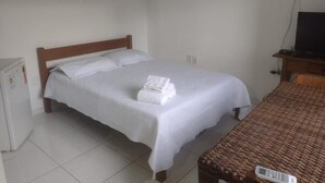 Una cama individual con cabecera de madera, una mesita de noche pequeña y un televisor sobre un soporte.