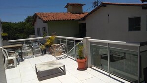 Una terraza en la azotea con barandilla de cristal, mobiliario exterior y plantas en macetas.