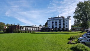 A large building with multiple floors, a flat roof, and a parking area with cars. - Hostel Oslofjord (Bærum)