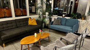 A living room with a dark grey sofa, a blue sofa, two wooden coffee tables, and a wire chair with a patterned cushion. - Hostel Oslofjord (Bærum)