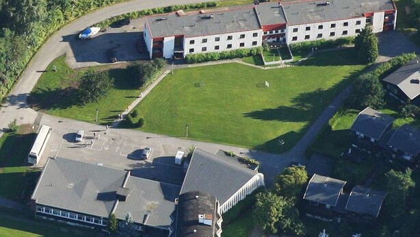 An aerial view of a building with a parking lot, a green lawn, and adjacent residential houses. - Hostel Oslofjord (Bærum)