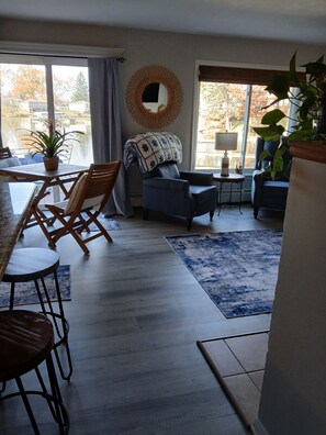 A living room with a dining area, a large mirror, and a view of a body of water.
