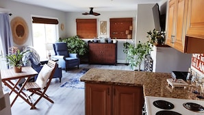 A modern kitchen with granite countertops, a built-in stove, and wooden cabinets. There is a dining area with a blue chair and a small table.