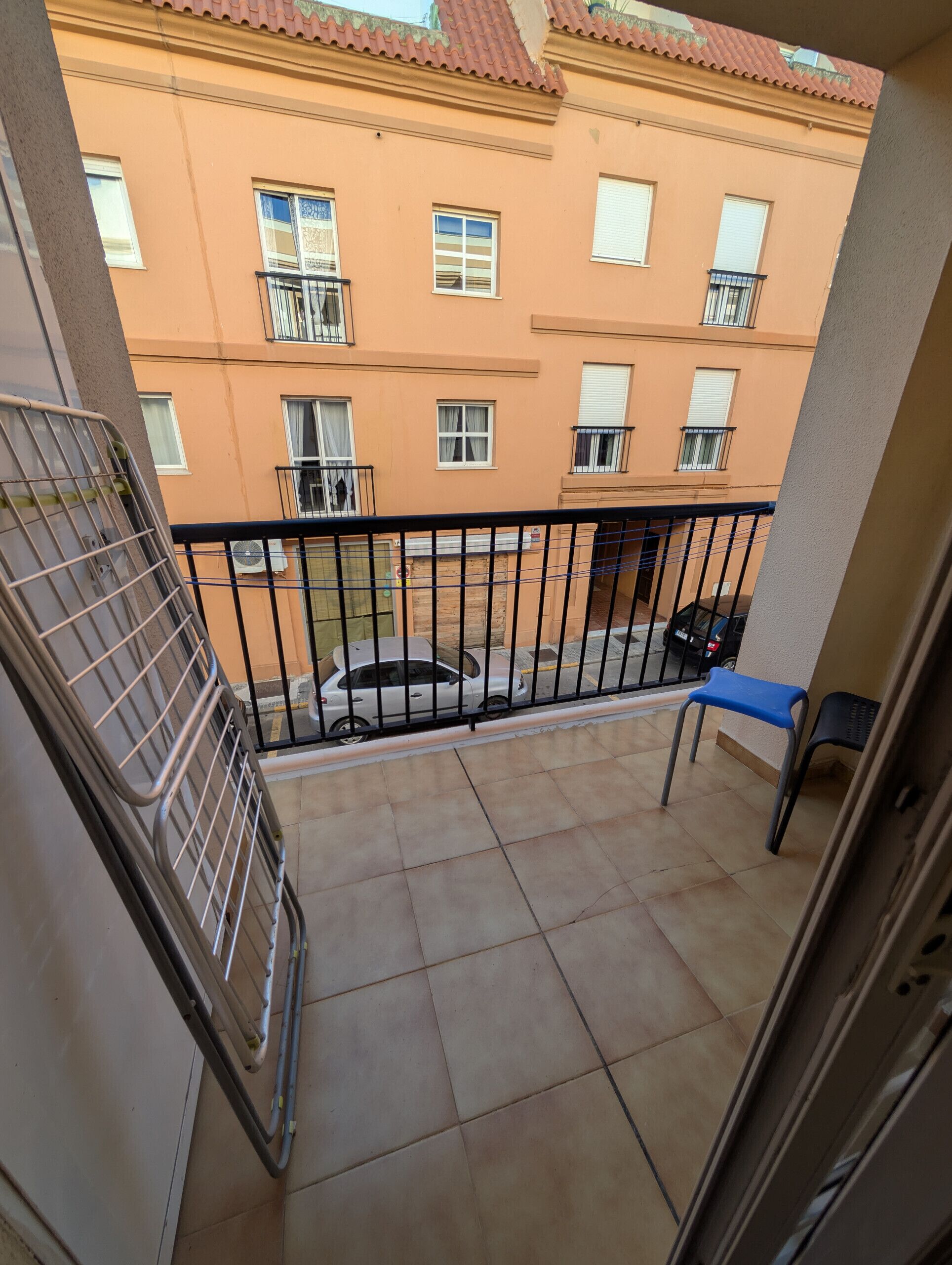 A balcony with a tiled floor, a metal railing, a blue chair, and a parked car.