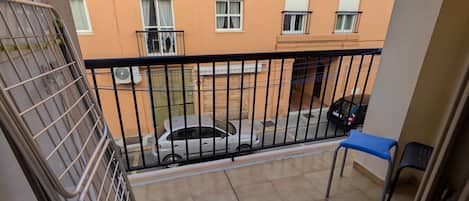 A balcony with a tiled floor, a metal railing, a blue chair, and a parked car.