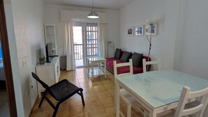 Un vaste espace de vie comprenant une table à manger avec un plateau en verre, des chaises blanches, un canapé rouge et un fauteuil noir.