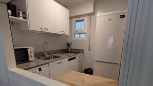 Une cuisine compacte avec des meubles blancs, un four à micro-ondes, un évier et une fenêtre au-dessus du plan de travail.