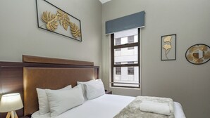 Camera d'albergo con un letto grande, un comodino con una lampada, una finestra con tende e decorazioni alle pareti.