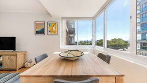 A modern dining area with a wooden table, chairs, and a large window offering a city view.