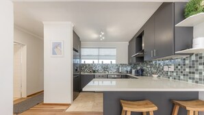 A modern kitchen with dark cabinets, a large island with stools, and a tiled backsplash.