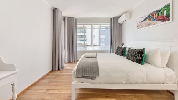 A bedroom with a large bed, a view of buildings through the window, and a painting on the wall.