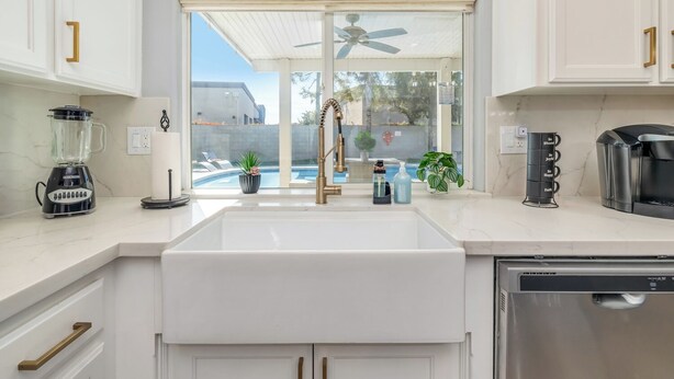 A modern kitchen with white cabinetry, a built-in dishwasher, a coffee maker, and a view of a swimming pool. - Spacious 4-bedroom house with Pool, Fun BackYard & Amazing Game Room (Bakersfield)