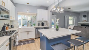 A modern kitchen with white cabinets, a central island, and bar stools. - Spacious 4-bedroom house with Pool, Fun BackYard & Amazing Game Room (Bakersfield)