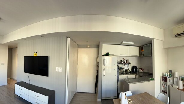 A modern living room with a flat-screen TV, a sofa, and a dining area with a table and chairs. A kitchen with a refrigerator and a microwave is visible in the background. - Ambientes Baires (Buenos Aires)