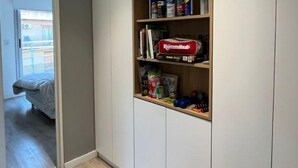 A hallway with a built-in wardrobe, a wooden shelf with various items, and a door leading to another room. - Ambientes Baires (Buenos Aires)