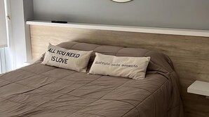 A bedroom with a bed, two pillows, a round mirror, and a bedside table. - Ambientes Baires (Buenos Aires)