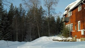 Un paisaje nevado con un edificio de madera y un bosque al fondo.