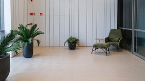 A modern lobby with a high ceiling, vertical paneling, and hanging spherical lights. There are two potted plants and a green armchair. - ON Augusta (São Paulo)