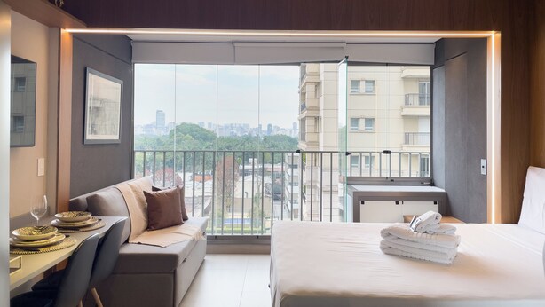 A modern hotel room with a balcony, a dining area, and a bed with towels. - ON Augusta (São Paulo)