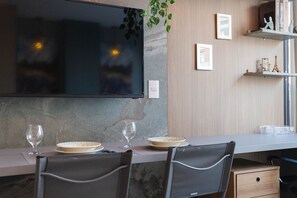 Uma cozinha moderna com uma televisão de tela plana grande, uma mesa de jantar posta com pratos e copos, e uma planta pendurada.